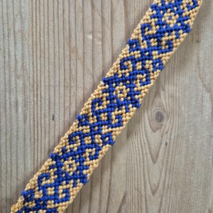 May include: A blue and gold friendship bracelet with a geometric pattern.