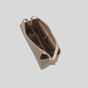Pode incluir: Organizador de bolsa de feltro bege com v&aacute;rios compartimentos e um bolso com z&iacute;per. O organizador &eacute; projetado para caber dentro de uma bolsa maior, ajudando a manter os itens organizados.