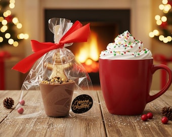 May include: A festive holiday scene featuring a red mug filled with whipped cream and sprinkles, and a chocolate treat in a clear bag tied with a red bow. A gingerbread man sits atop a chocolate cup filled with candies. The words "Merry Christmas" are on a black sticker.