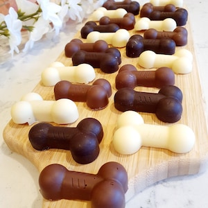 May include: A wooden board with a variety of chocolate dog bone treats. The treats are in two colors: white chocolate and dark chocolate.