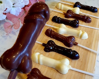 May include: A close-up of a wooden board with chocolate lollipops in various colors, including brown, white, and black. The lollipops are shaped like a bone and are arranged in a row on the board.