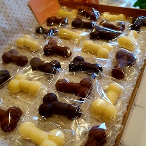 May include: A variety of chocolate candies shaped like bones, individually wrapped in clear plastic and arranged in a wooden tray. The candies are in shades of brown and white.