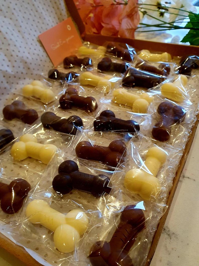 May include: A variety of chocolate candies shaped like bones, individually wrapped in clear plastic and arranged in a wooden tray. The candies are in shades of brown and white.