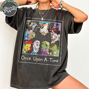 Puede incluir: Camiseta gris oscuro con un gr&aacute;fico cuadrado con personajes de dibujos animados y el texto "Once Upon A Time". El gr&aacute;fico incluye personajes como Ariel, Olaf y Rapunzel. La camiseta tiene una etiqueta Comfort Colors Pepper.