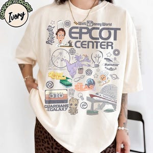 Könnte beinhalten: Elfenbeinfarbenes T-Shirt mit einem grafischen Design mit dem Text "EPCOT CENTER" und verschiedenen Illustrationen. Das Design enthält Bilder von Charakteren und Attraktionen aus Walt Disney World, wie Figment und Guardians of the Galaxy.