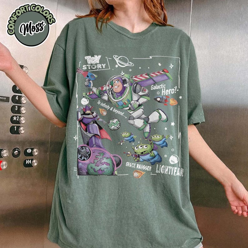Puede incluir: Una camiseta de manga corta color verde musgo con un estampado gr&aacute;fico de Buzz Lightyear y otros personajes de Toy Story. El dise&ntilde;o incluye el texto "Toy Story", "Galactic Hero!", "To infinity & beyond..." y "Space Ranger Lightyear."