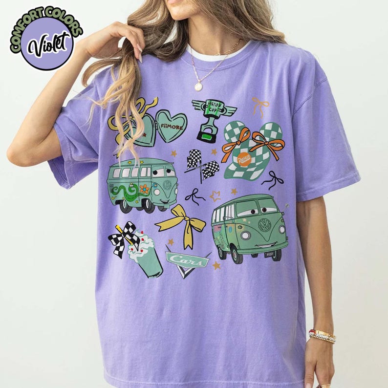 Puede incluir: Una camiseta violeta Comfort Colors con gr&aacute;ficos de dibujos animados de furgonetas verdes, corazones, lazos y un trofeo. La camiseta incluye el texto "Cars" y "Filmore". El dise&ntilde;o tiene una est&eacute;tica l&uacute;dica y caprichosa.