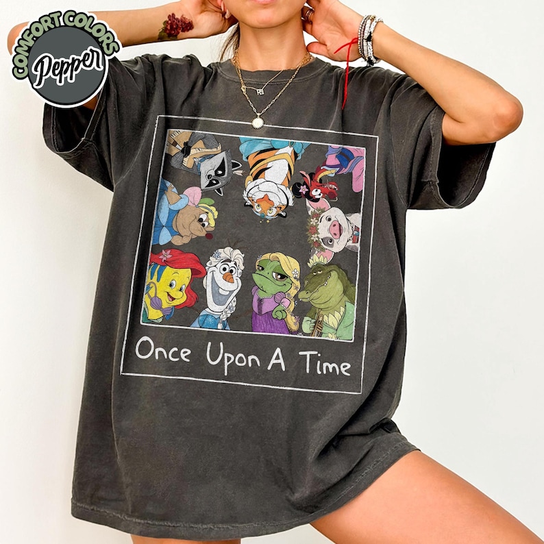 Puede incluir: Camiseta gris oscuro con un gr&aacute;fico cuadrado con personajes de dibujos animados y el texto "Once Upon A Time". El gr&aacute;fico incluye personajes como Ariel, Olaf y Rapunzel. La camiseta tiene una etiqueta Comfort Colors Pepper.