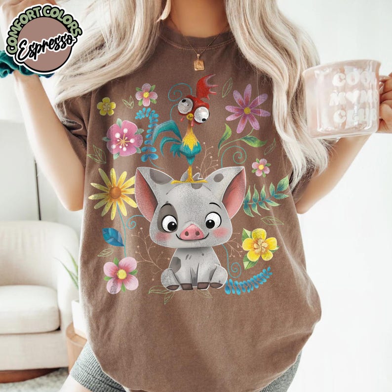 May include: Brown t-shirt featuring a cartoon pig and rooster surrounded by colorful flowers and vines. The shirt has the text "Comfort Colors Espresso" in a circular design on the upper left.