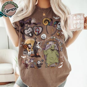 May include: Brown t-shirt featuring a colorful graphic of characters and elements from "The Nightmare Before Christmas." The design includes Jack Skellington, Sally, Oogie Boogie, and other iconic imagery. The shirt has a crew neck and short sleeves.