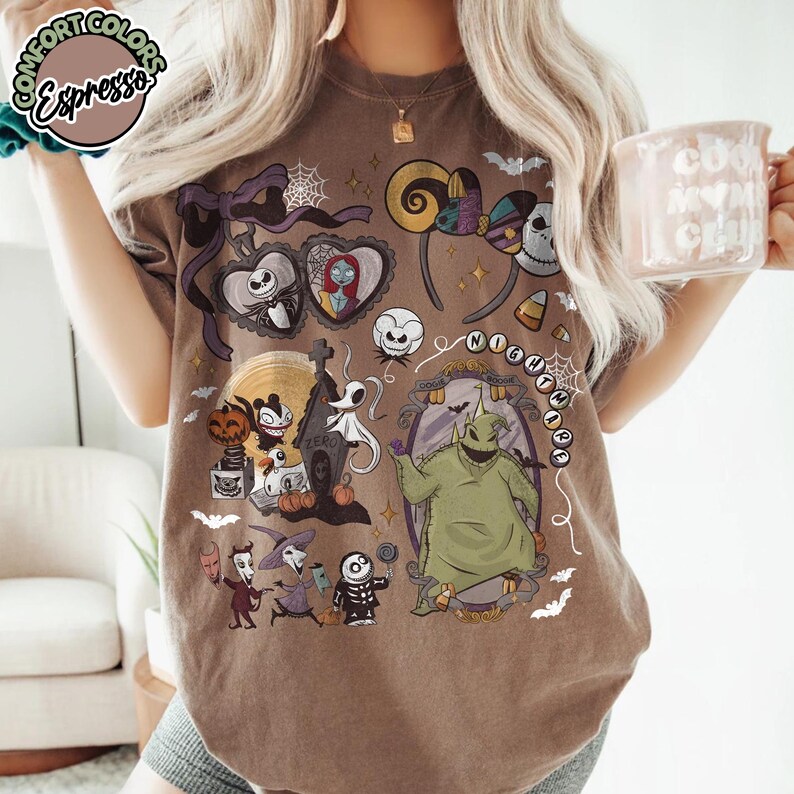 May include: Brown t-shirt featuring a colorful graphic of characters and elements from "The Nightmare Before Christmas." The design includes Jack Skellington, Sally, Oogie Boogie, and other iconic imagery. The shirt has a crew neck and short sleeves.