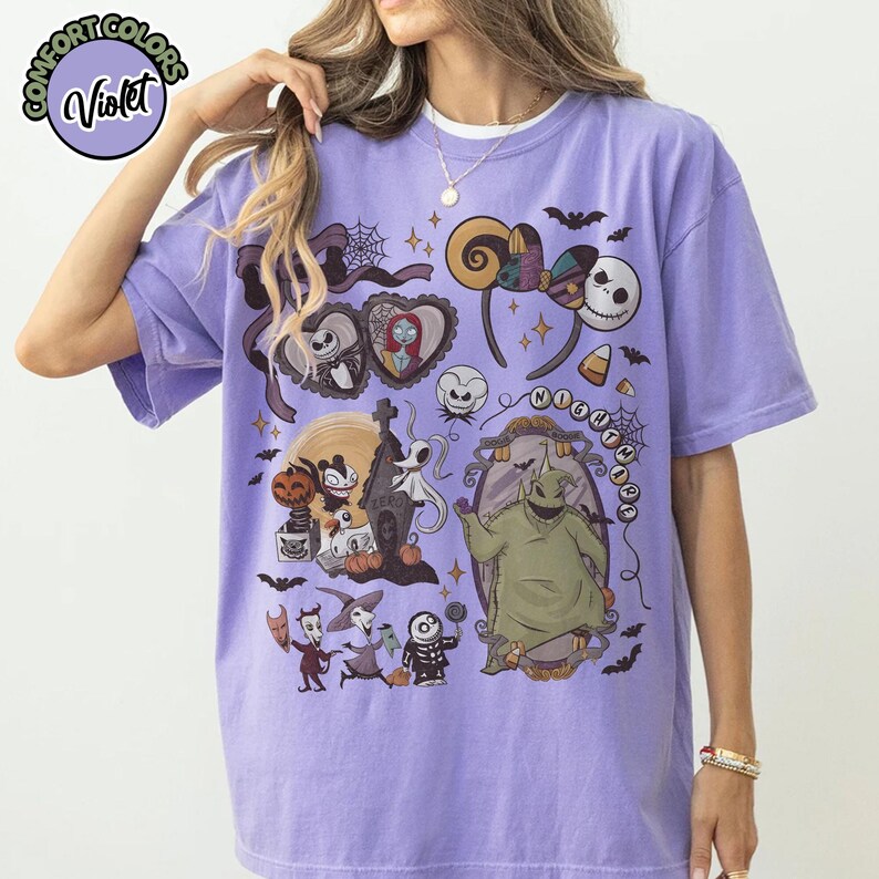 May include: Violet Comfort Colors t-shirt featuring a colorful graphic design with characters and elements from "The Nightmare Before Christmas." The design includes Jack Skellington, Sally, Oogie Boogie, and other iconic imagery. The text "NIGHTMARE" is also visible.