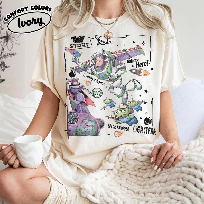 Puede incluir: Una camiseta de color marfil con un estampado gr&aacute;fico de Buzz Lightyear, Zurg y alien&iacute;genas de Toy Story. El dise&ntilde;o incluye el texto "Toy Story", "Galactic Hero!", "To infinity & beyond....", "Space Ranger" y "Lightyear" con elementos espaciales.