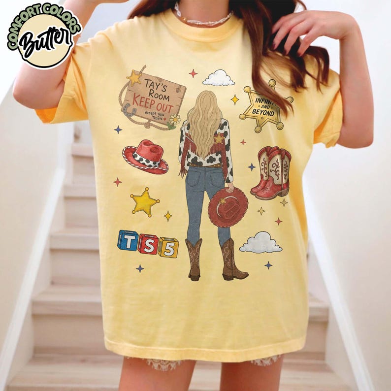 May include: A pale yellow t-shirt featuring a graphic of a person with long blonde hair seen from behind, wearing a cow-print jacket, blue jeans, and brown boots. The design includes a sign reading Tay's Room Keep Out, a sheriff badge, cowboy hat, boots, and TS5 blocks.