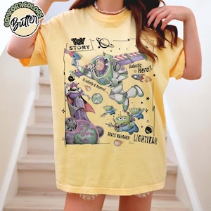 Puede incluir: Una camiseta de color amarillo p&aacute;lido con un estampado gr&aacute;fico de Buzz Lightyear, Zurg y alien&iacute;genas de Toy Story. El dise&ntilde;o incluye el texto "Toy Story", "Galactic Hero!", "To infinity & beyond....", "Space Ranger" y "Lightyear" con motivos espaciales.