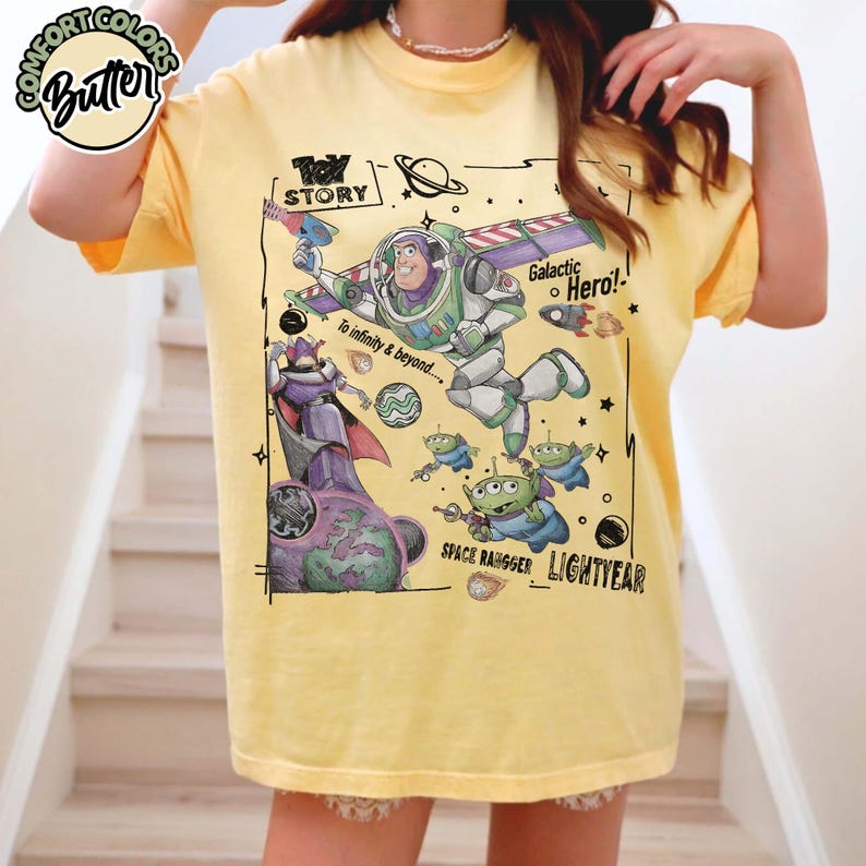 Puede incluir: Una camiseta de color amarillo p&aacute;lido con un estampado gr&aacute;fico de Buzz Lightyear, Zurg y alien&iacute;genas de Toy Story. El dise&ntilde;o incluye el texto "Toy Story", "Galactic Hero!", "To infinity & beyond....", "Space Ranger" y "Lightyear" con motivos espaciales.