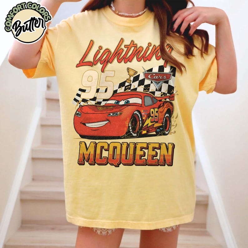 Pu&ograve; includere: T-shirt giallo chiaro con una grafica di Saetta McQueen del film Cars. Il design include il testo "Lightning 95 McQueen" con una bandiera a scacchi e un trofeo. La maglietta ha maniche corte e una vestibilit&agrave; ampia.