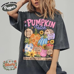 May include: A charcoal gray t-shirt featuring a graphic print with the text PUMPKIN Patch, Fresh from the Patch, Farm Fresh, Locally Grown, Autumn Picked, Pumpkins, Corn Maze, and Apple Cider, alongside illustrations of pumpkins and sunflowers.