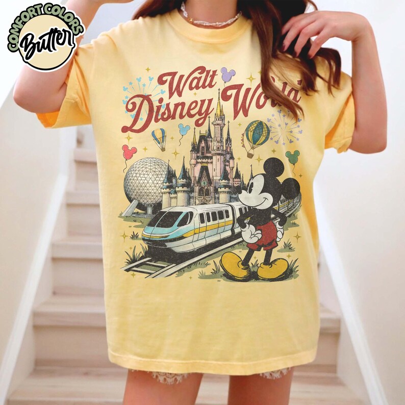 May include: Yellow t-shirt with a Walt Disney World graphic featuring Mickey Mouse, a castle, and a monorail. The design includes fireworks and hot air balloons. The text "Walt Disney World" is in a retro font.