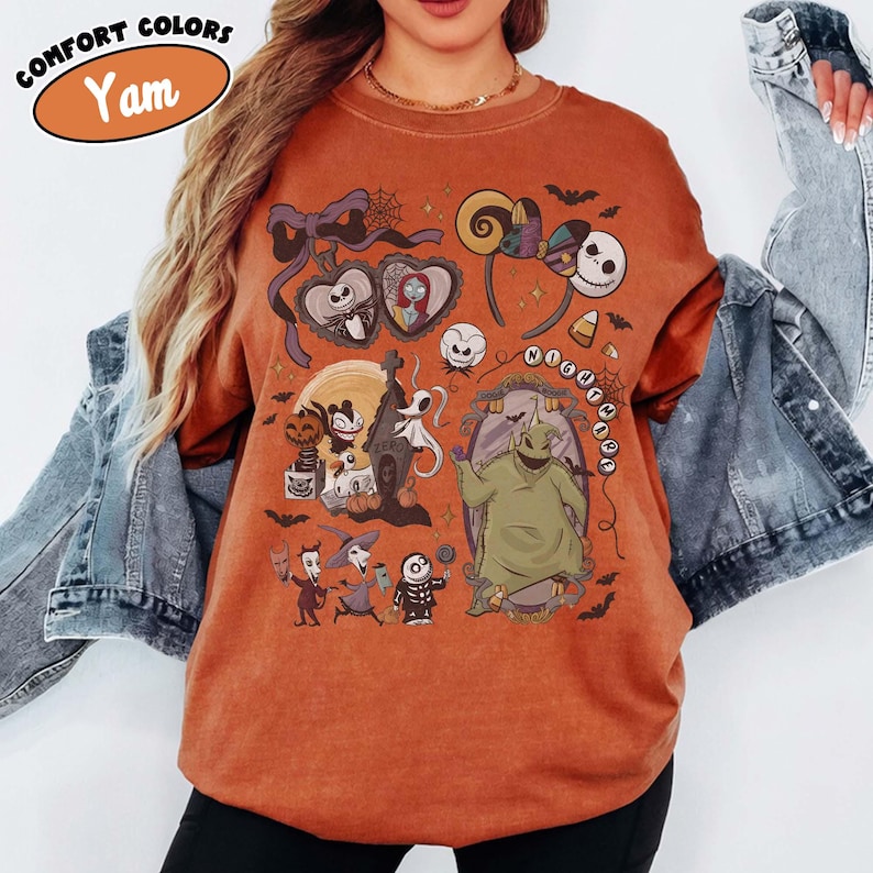 May include: Orange-colored t-shirt with a graphic featuring characters and elements from "The Nightmare Before Christmas." The design includes Jack Skellington, Sally, Oogie Boogie, and other spooky elements. The shirt has the text "Comfort Colors" and "Yam."