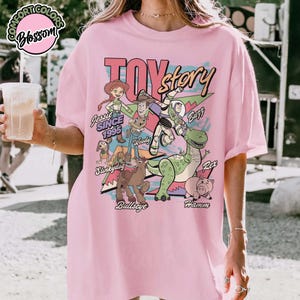 May include: Pink t-shirt featuring the words "Toy Story" in a retro font, with cartoon characters Jessie, Woody, Buzz Lightyear, Rex, Hamm, Slinky Dog, and Bullseye. The text "Since 1995" is also included.