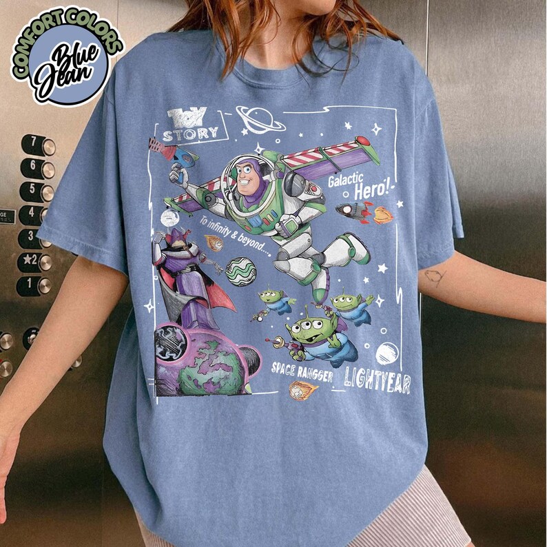 Puede incluir: Una camiseta azul de manga corta con un gr&aacute;fico de Toy Story que muestra a Buzz Lightyear, Zurg y alien&iacute;genas. El estampado incluye el texto Toy Story, Galactic Hero, To infinity & beyond, Space Ranger y Lightyear, rodeado de estrellas.