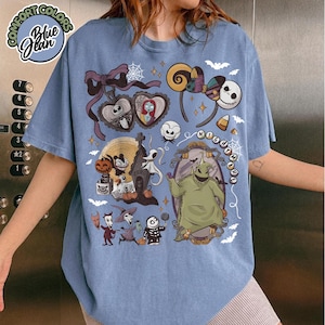 May include: Blue graphic t-shirt featuring characters from The Nightmare Before Christmas. The design includes Jack Skellington, Sally, Oogie Boogie, and Zero. The shirt has the words "NIGHTMARE" and "Blue Jean" printed on it.