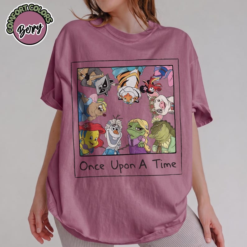 Puede incluir: Una camiseta de color malva con un dise&ntilde;o gr&aacute;fico enmarcado de personajes de dibujos animados, como un mapache, un tigre y un cerdo. La frase "Once Upon A Time" est&aacute; impresa debajo. La camiseta tiene mangas cortas y un corte holgado.
