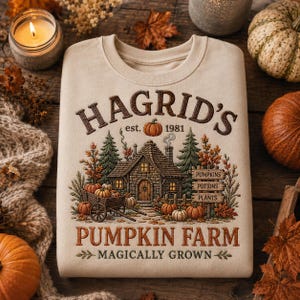 Peut inclure: Un sweat-shirt beige à col rond orné d'une illustration de cottage en pierre entouré de sapins et de citrouilles. Le texte indique HAGRID'S est. 1981 PUMPKIN FARM MAGICALLY GROWN, avec un panneau en bois listant PUMPKINS, POTIONS et PLANTS.