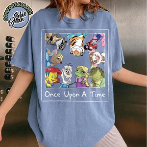Puede incluir: Camiseta azul vaquero con un gr&aacute;fico enmarcado de personajes de dibujos animados, incluyendo un mapache, un tigre y un cerdo. El texto "Once Upon A Time" est&aacute; debajo. La camiseta tiene cuello redondo y mangas cortas.