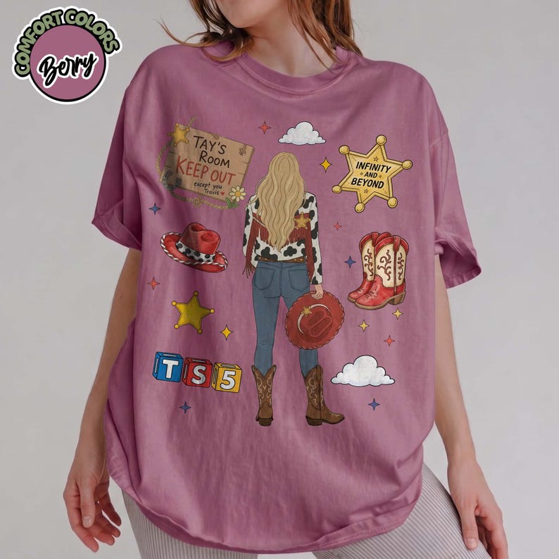 May include: A berry-coloured t-shirt featuring a graphic of a person with long blonde hair wearing a cow-print jacket, blue jeans, and brown boots. The design includes a sign reading Tay's Room Keep Out, a star labelled Infinity and Beyond, and blocks.
