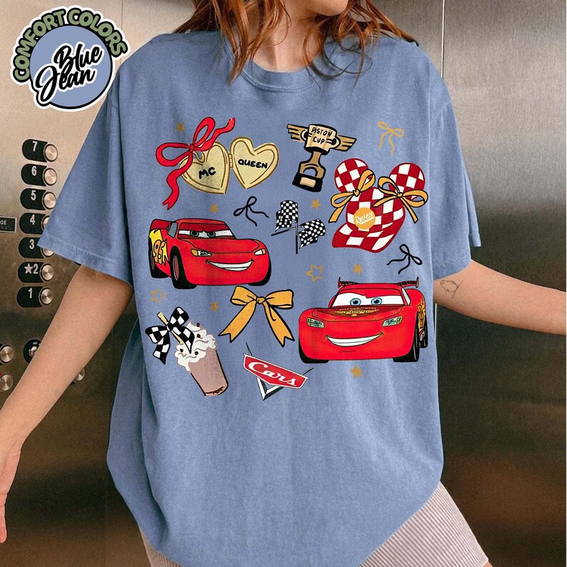 Puede incluir: Camiseta azul Comfort Colors con un dise&ntilde;o de la pel&iacute;cula Cars. El dise&ntilde;o incluye a Rayo McQueen, banderas de carreras y el texto "Cars". La camiseta tambi&eacute;n tiene el texto "Blue Jean" y "Comfort Colors".