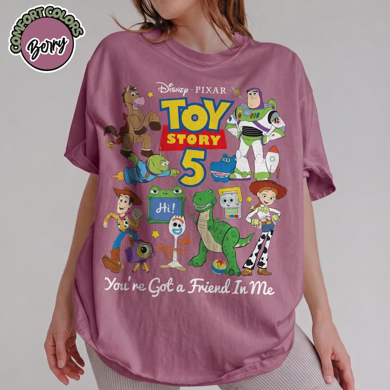 May include: A berry-colored t-shirt featuring a graphic print of Disney Pixar Toy Story characters including Woody, Buzz Lightyear, Jessie, Rex, and Forky. The design includes the text Toy Story 5 and the phrase You're Got a Friend In Me.