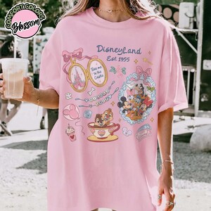 Peut inclure: T-shirt rose clair avec un motif Disneyland. Le design comprend une montre de poche avec un ch&acirc;teau, Mickey Mouse, Donald Duck, Tic et Tac, et le texte "Take me to the Castle". Le t-shirt porte &eacute;galement l'inscription "Disneyland Est. 1955".