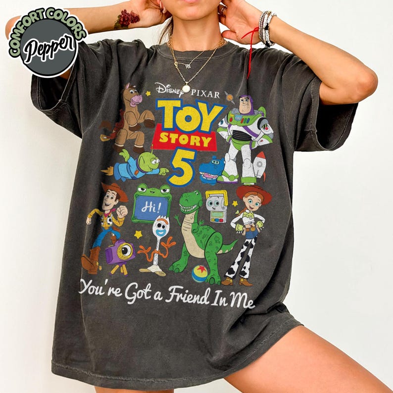 May include: A charcoal gray short-sleeve t-shirt featuring a graphic print of Disney Pixar Toy Story characters including Woody, Buzz Lightyear, Jessie, Rex, and Forky. The design includes the text Toy Story 5 and You're Got a Friend In Me.