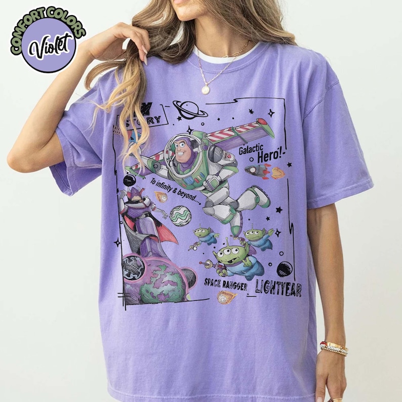 Puede incluir: Una camiseta violeta de manga corta con un estampado gr&aacute;fico de Buzz Lightyear, Zurg y alien&iacute;genas verdes. El texto dice "Toy Story", "Galactic Hero!", "To infinity & beyond....", "Space Ranger" y "Lightyear" con ilustraciones de tem&aacute;tica espacial.