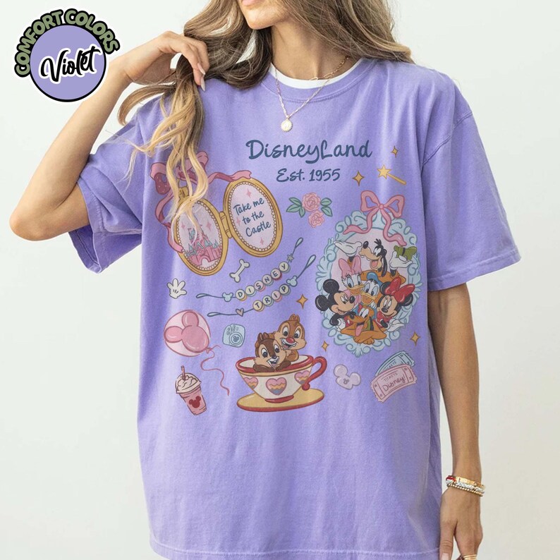 Peut inclure: Un t-shirt violet Comfort Colors avec des graphismes de Disneyland. Le design comprend Mickey Mouse, Minnie Mouse, Dingo et Donald Duck. Le t-shirt porte &eacute;galement l'inscription "Disneyland Est. 1955" et d'autres illustrations sur le th&egrave;me de Disney.