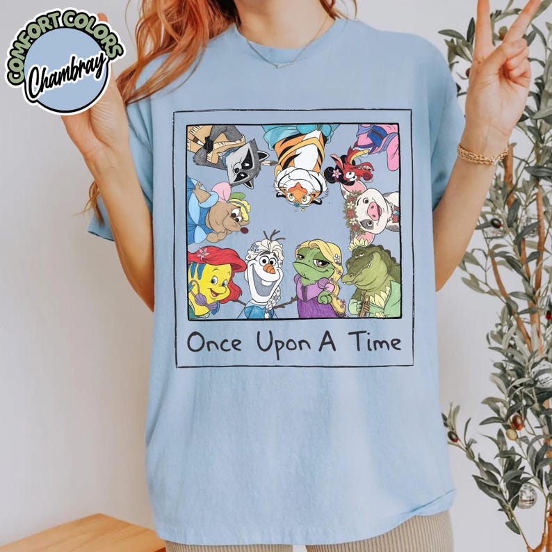 Puede incluir: Camiseta azul claro con una ilustraci&oacute;n enmarcada de personajes de dibujos animados, como un mapache, un tigre y una rana. La frase "Once Upon A Time" est&aacute; escrita debajo. La camiseta tiene mangas cortas y cuello redondo.