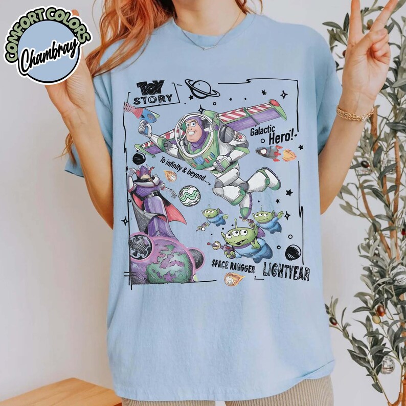 Puede incluir: Una camiseta azul claro con un estampado gr&aacute;fico de Buzz Lightyear, Zurg y alien&iacute;genas verdes de Toy Story. El dise&ntilde;o incluye el texto Toy Story, Galactic Hero, To infinity & beyond, Space Ranger y Lightyear en un estilo de boceto negro.