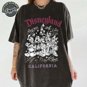 Puede incluir: Camiseta gris oscuro con un dise&ntilde;o de Disneyland que presenta a Mickey Mouse, Goofy, Daisy Duck, Donald Duck, Pluto y Minnie Mouse. El texto "Disneyland California" est&aacute; impreso en una fuente estilizada. La camiseta tiene un aspecto vintage.