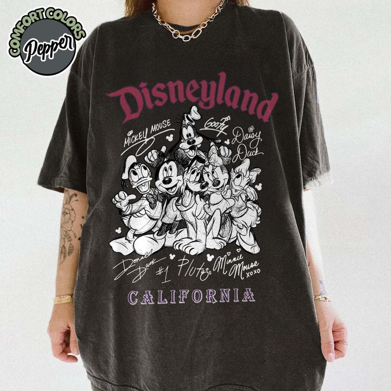 Puede incluir: Camiseta gris oscuro con un dise&ntilde;o de Disneyland que presenta a Mickey Mouse, Goofy, Daisy Duck, Donald Duck, Pluto y Minnie Mouse. El texto "Disneyland California" est&aacute; impreso en una fuente estilizada. La camiseta tiene un aspecto vintage.