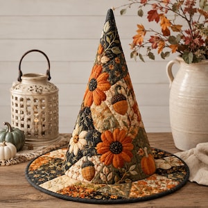 May include: A quilted witch hat featuring a patchwork design with autumn-themed motifs including orange sunflowers, brown acorns, and pumpkins. The fabric displays a color palette of black, cream, and burnt orange with intricate stitching throughout.
