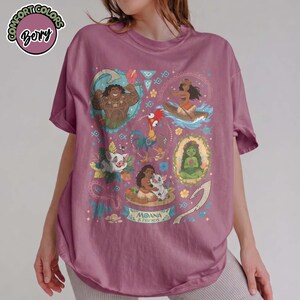 May include: A berry-colored short-sleeve t-shirt featuring a graphic print of Moana and friends, including Maui, Hei Hei, Pua, and Te Fiti. The design incorporates tropical floral elements, tribal patterns, and the text Moana & Friends.