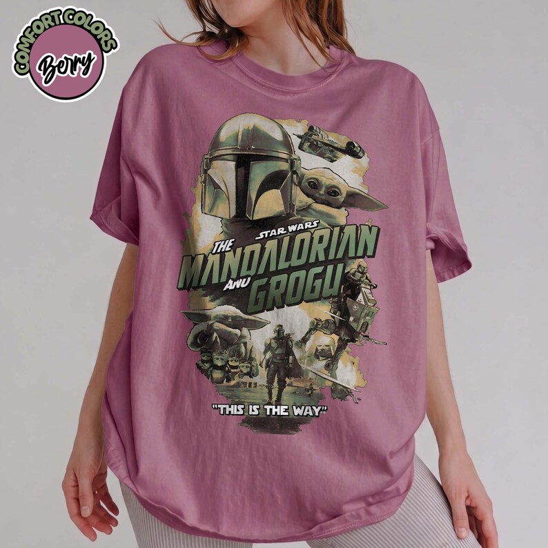 May include: A berry-colored t-shirt featuring a graphic print of The Mandalorian and Grogu. The design includes the text "The Mandalorian and Grogu" and "This is the Way" alongside illustrations of the characters and a starship.