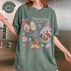 Peut inclure: T-shirt vert avec un motif Disneyland. Le motif comprend Mickey Mouse, Minnie Mouse, Donald Duck et Dingo. Le t-shirt comporte &eacute;galement le texte "Disneyland Est. 1955" et d'autres illustrations sur le th&egrave;me de Disney.