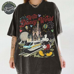 May include: Dark grey t-shirt with a colourful Walt Disney World graphic. The design includes the Disney World castle, Mickey Mouse, a monorail, and the text "Walt Disney World" in a vintage style. The shirt has a distressed, vintage appearance.