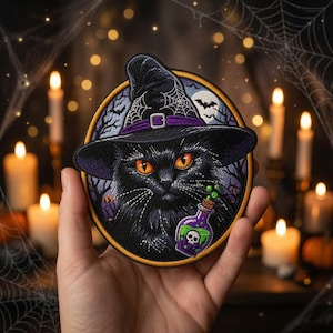 May include: A circular embroidered patch featuring a black cat wearing a pointed witch hat with a purple band. The background shows a night scene with a full moon, bats, and bare trees. The cat holds a small purple potion bottle with a skull.