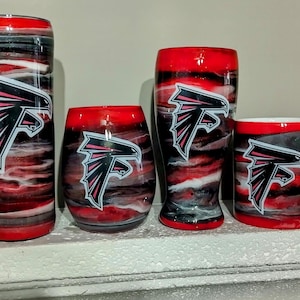 Puede incluir: Conjunto de cuatro vasos con un diseño de remolino rojo, negro y blanco con un logotipo de los Atlanta Falcons en rosa y negro.