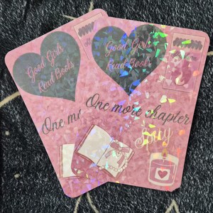 May include: Two pink stickers with holographic accents. One sticker features a heart with "Good Girls Read Books" and "One more chapter" text. The other sticker has similar text and illustrations of a book, candle, and other elements.