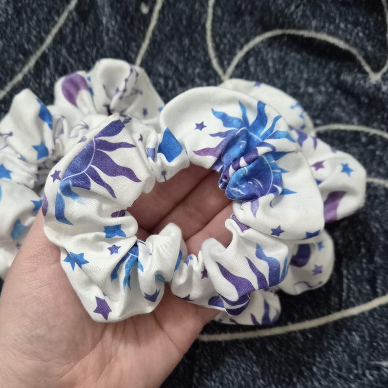Puede incluir: Coleteros blancos con un dise&ntilde;o celestial con soles y estrellas azules y moradas. La tela est&aacute; fruncida y el&aacute;stica, creando una apariencia texturizada. Estos accesorios para el cabello est&aacute;n dise&ntilde;ados para el uso diario.